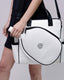 White handbag with black accents held by a person on a plain background