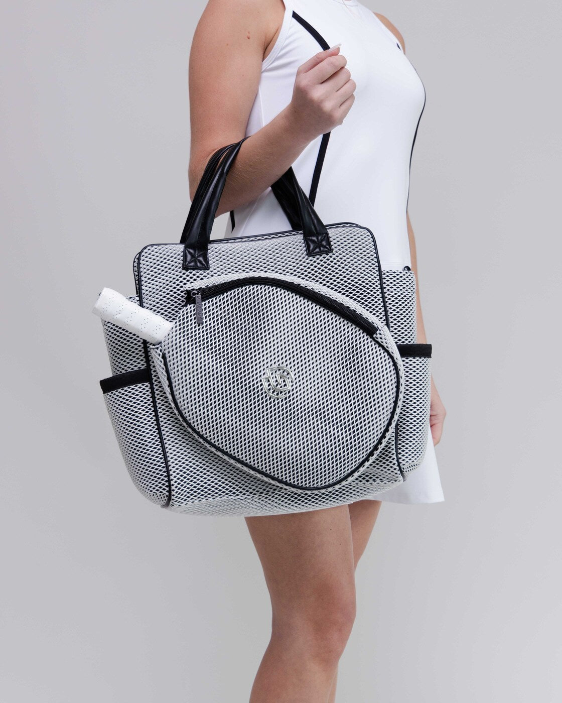 Person holding a black and white mesh bag with a visible brand logo on a plain background