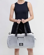 Person holding a white duffel bag with black accents on a light gray background