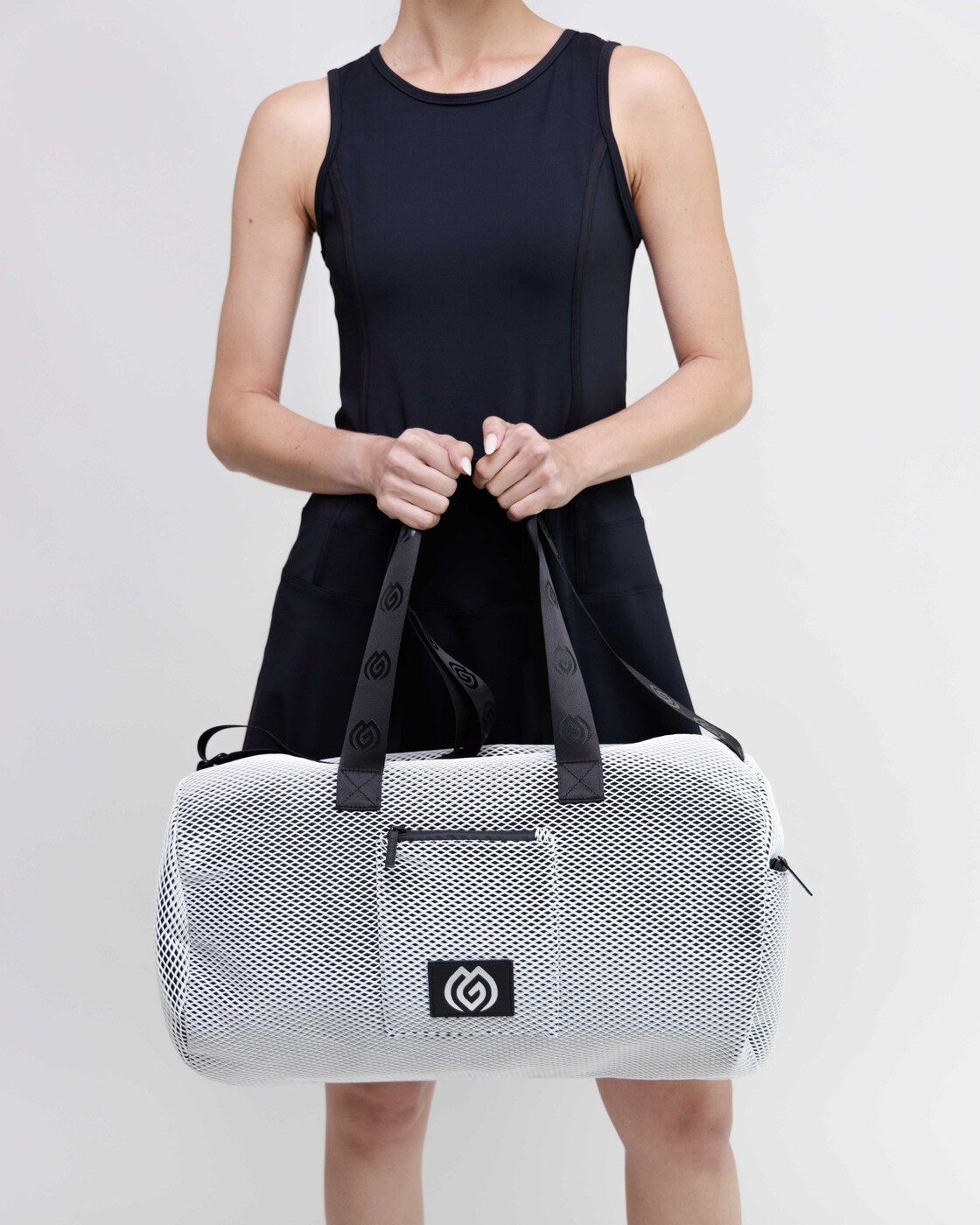 Person holding a white duffel bag with black accents on a light gray background