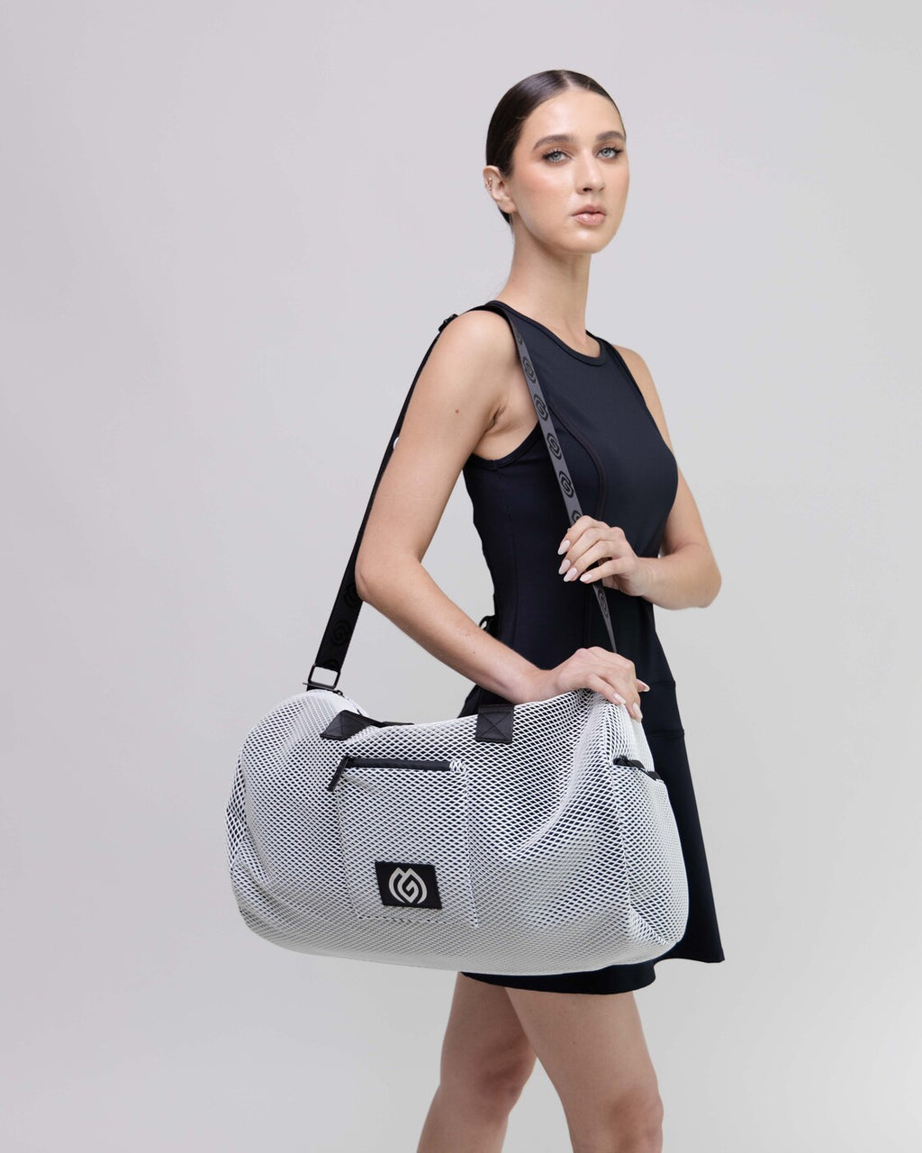 Woman holding a white mesh duffel bag with a brand logo on a light gray background