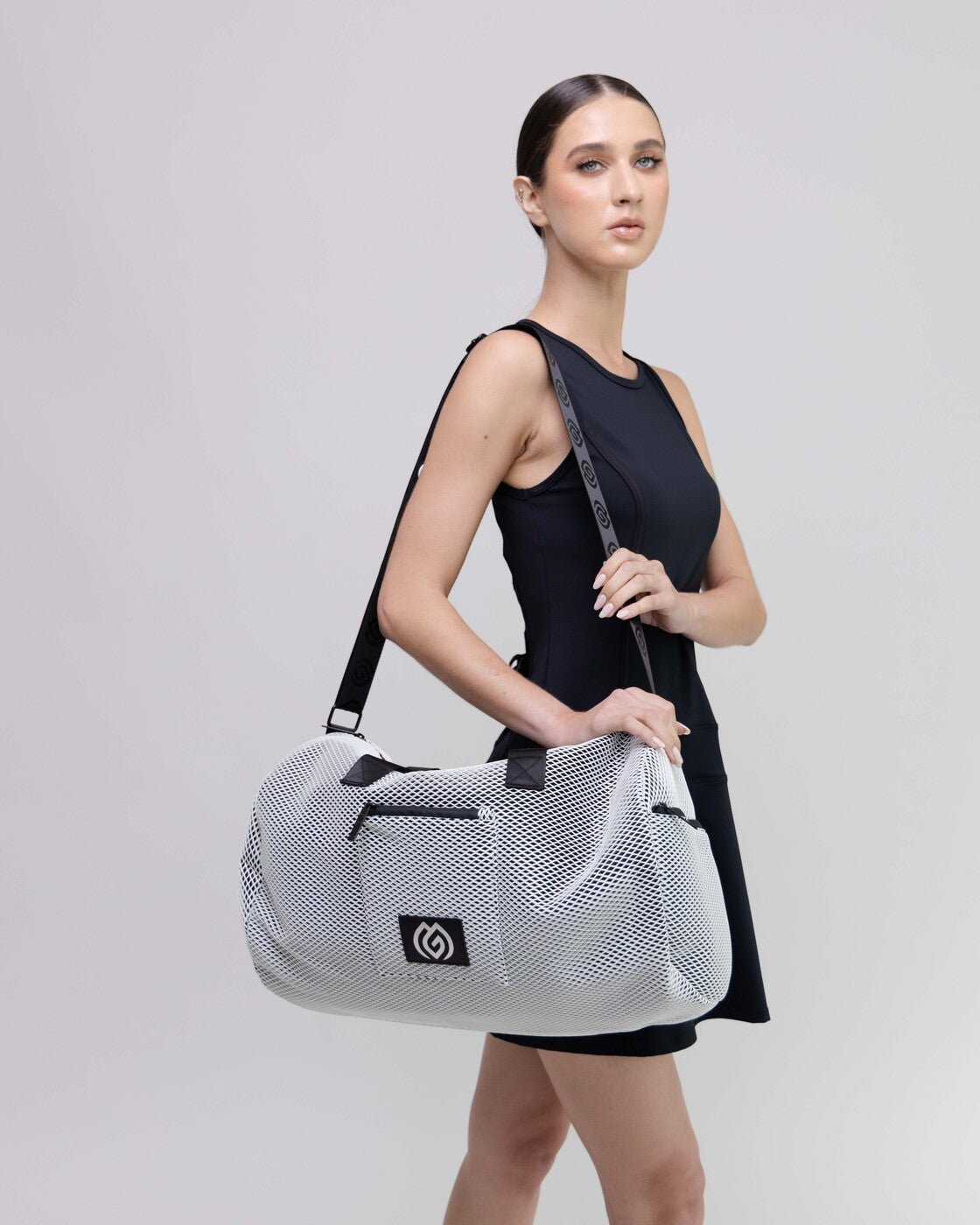 Woman holding a white mesh duffel bag with a brand logo on a light gray background