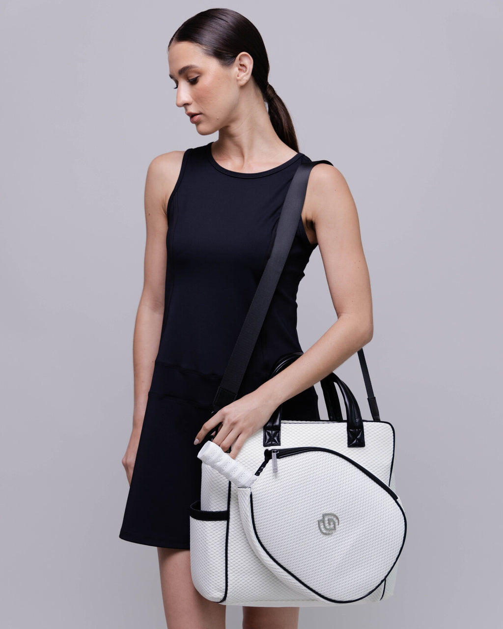 Woman holding a white bag with a black strap against a gray background