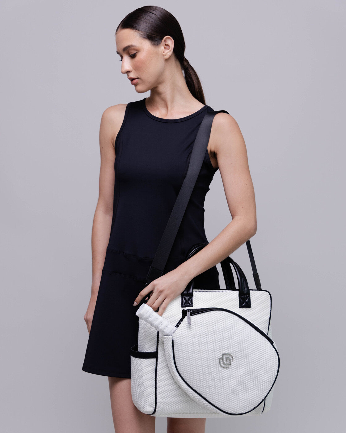 Woman holding a white bag with a black strap against a gray background