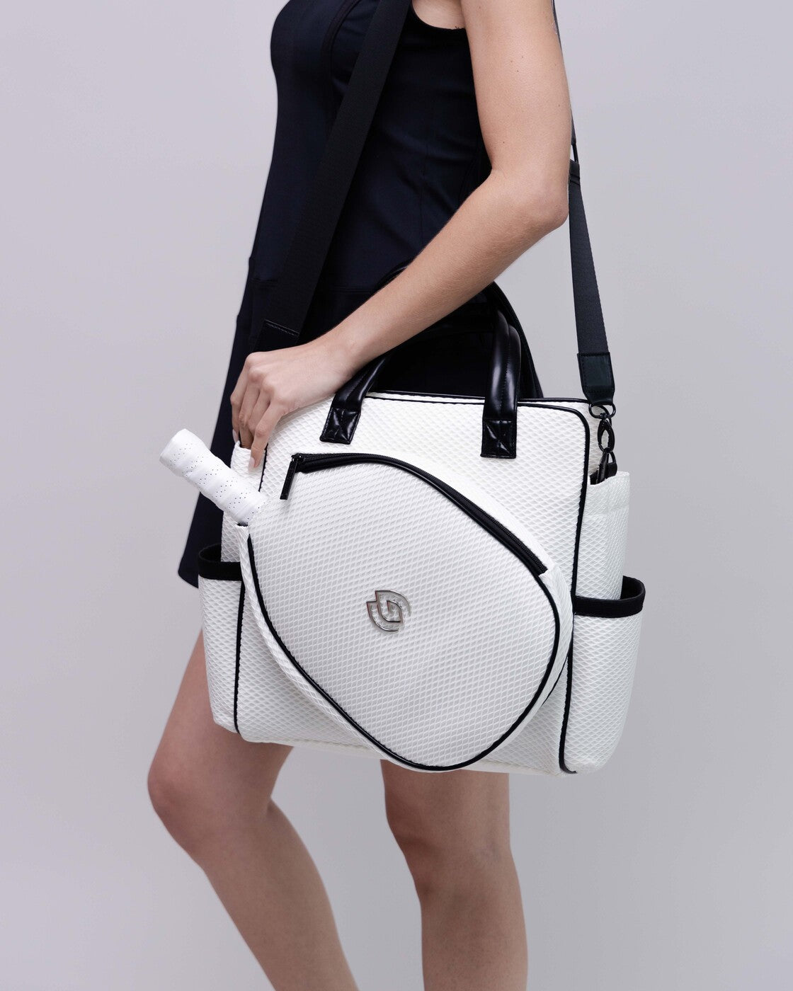 White handbag with black accents held by a person against a plain background