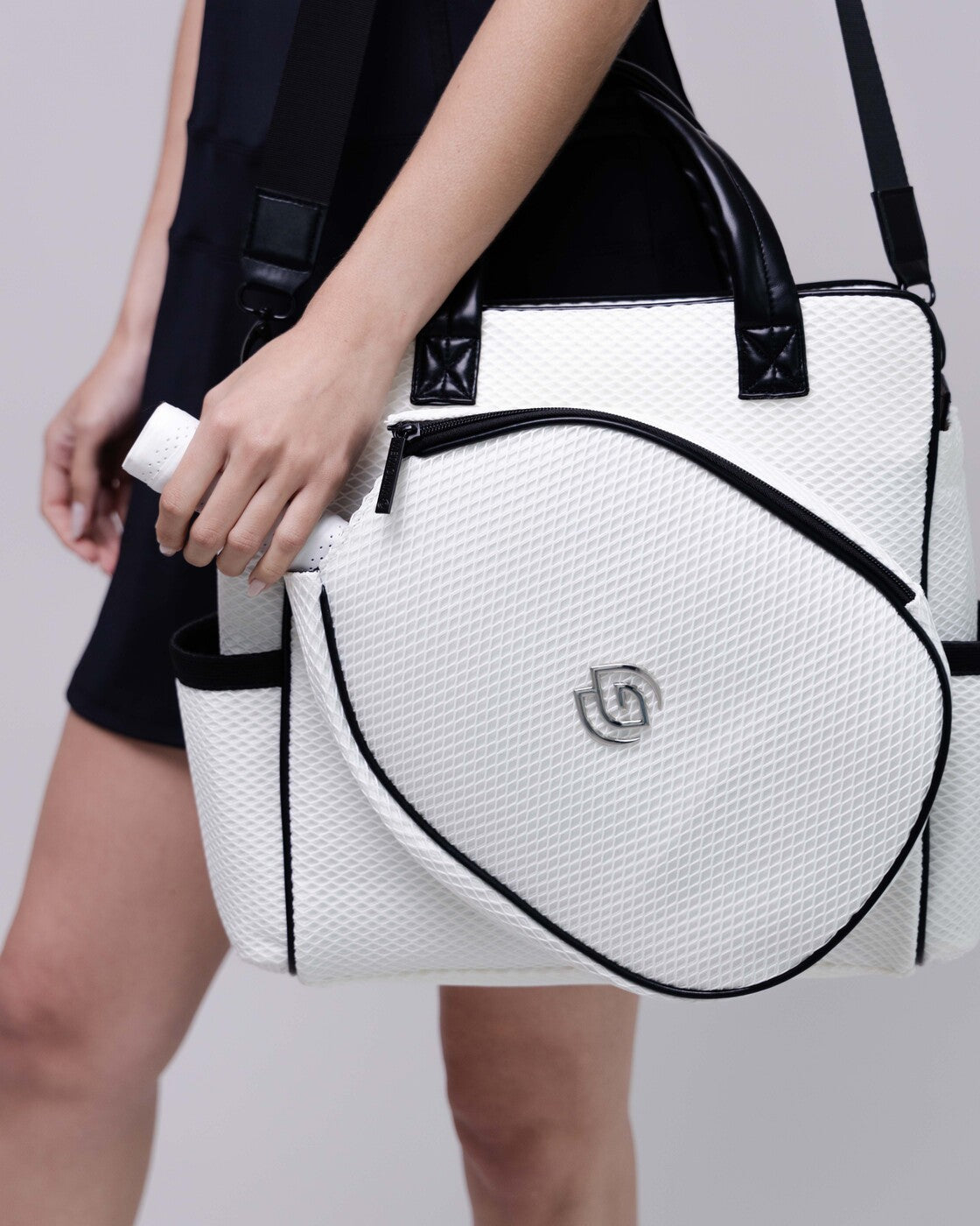 White handbag with black accents held by a person on a plain background