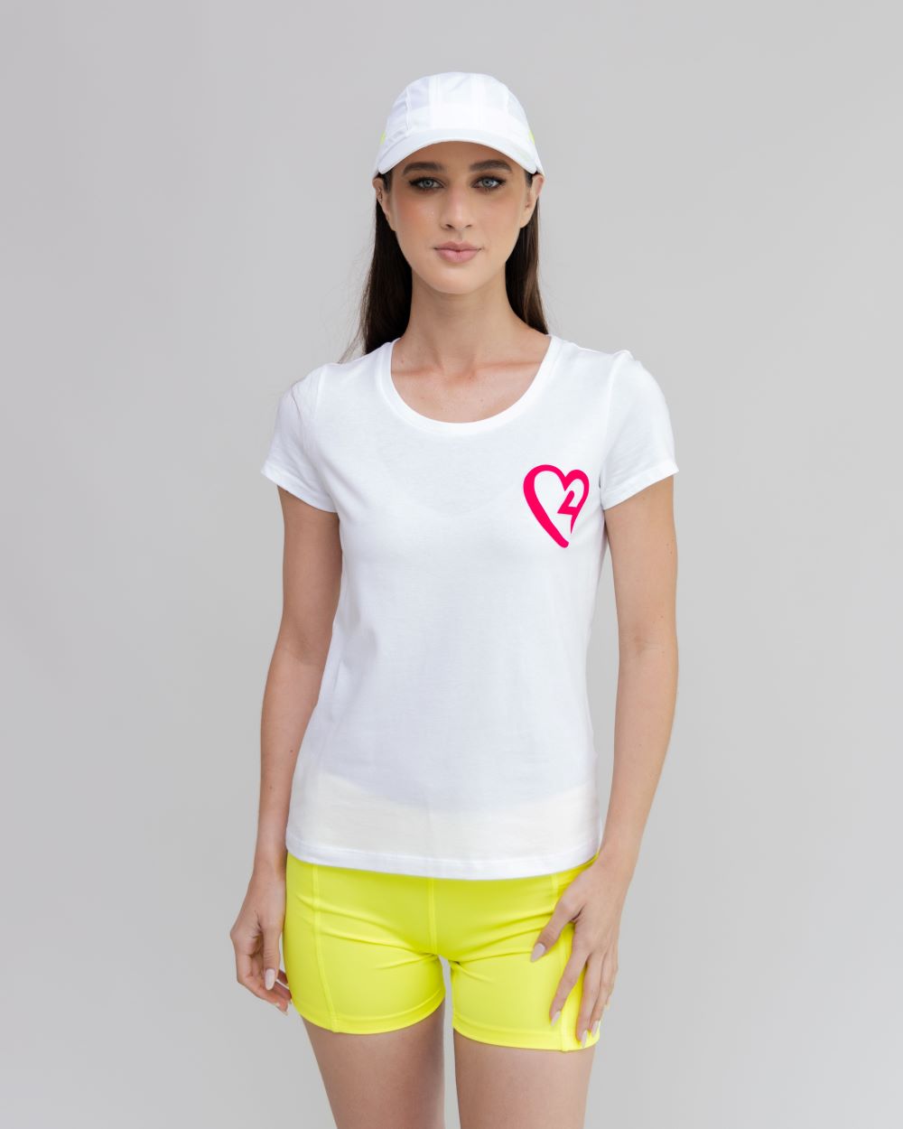 Woman wearing a white t-shirt with a pink heart design and yellow shorts on a gray background