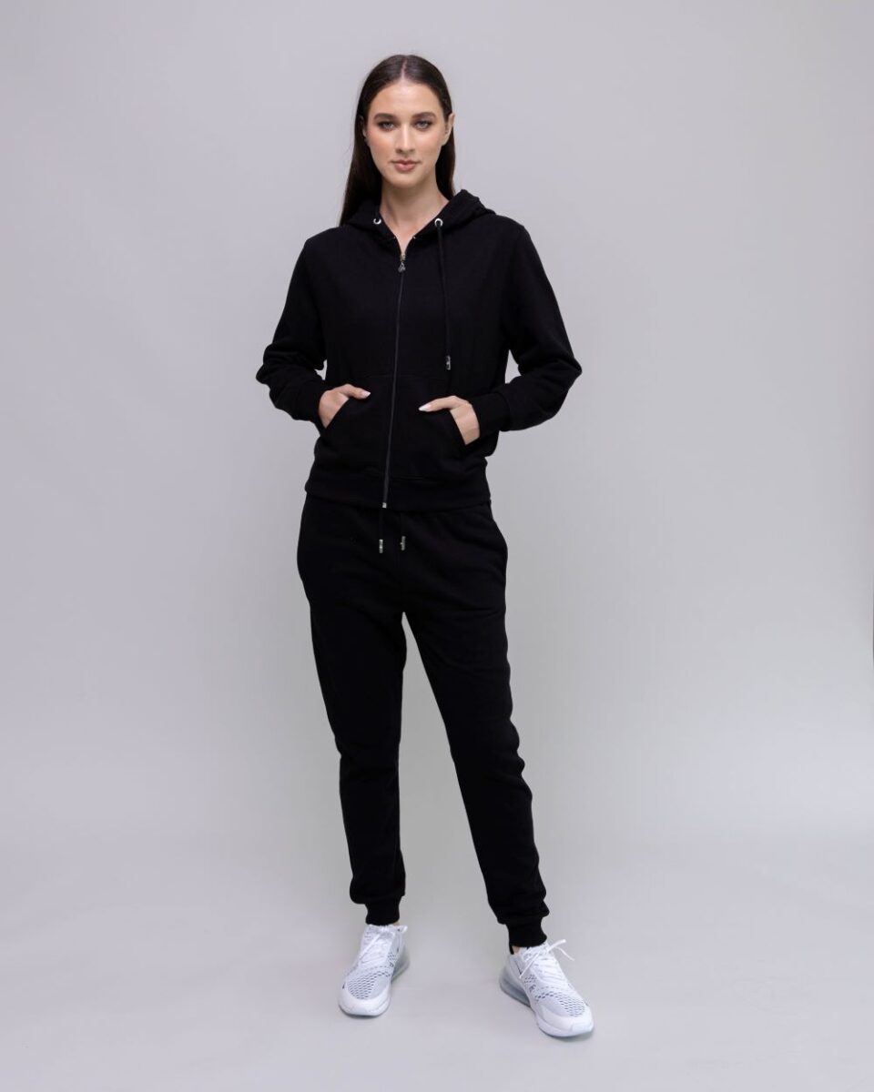 Person wearing a black tracksuit with white sneakers on a plain background