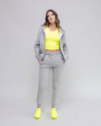 Woman wearing a gray tracksuit with a yellow top and shoes on a light gray background