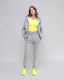 Woman wearing a gray tracksuit with a yellow top and shoes on a light gray background