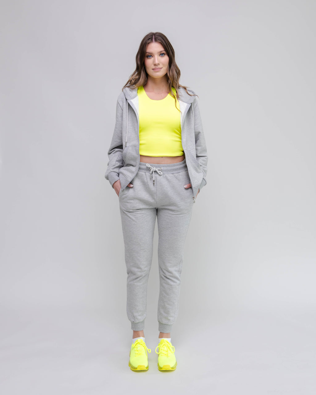 Woman wearing a gray tracksuit with a yellow top and shoes on a light gray background