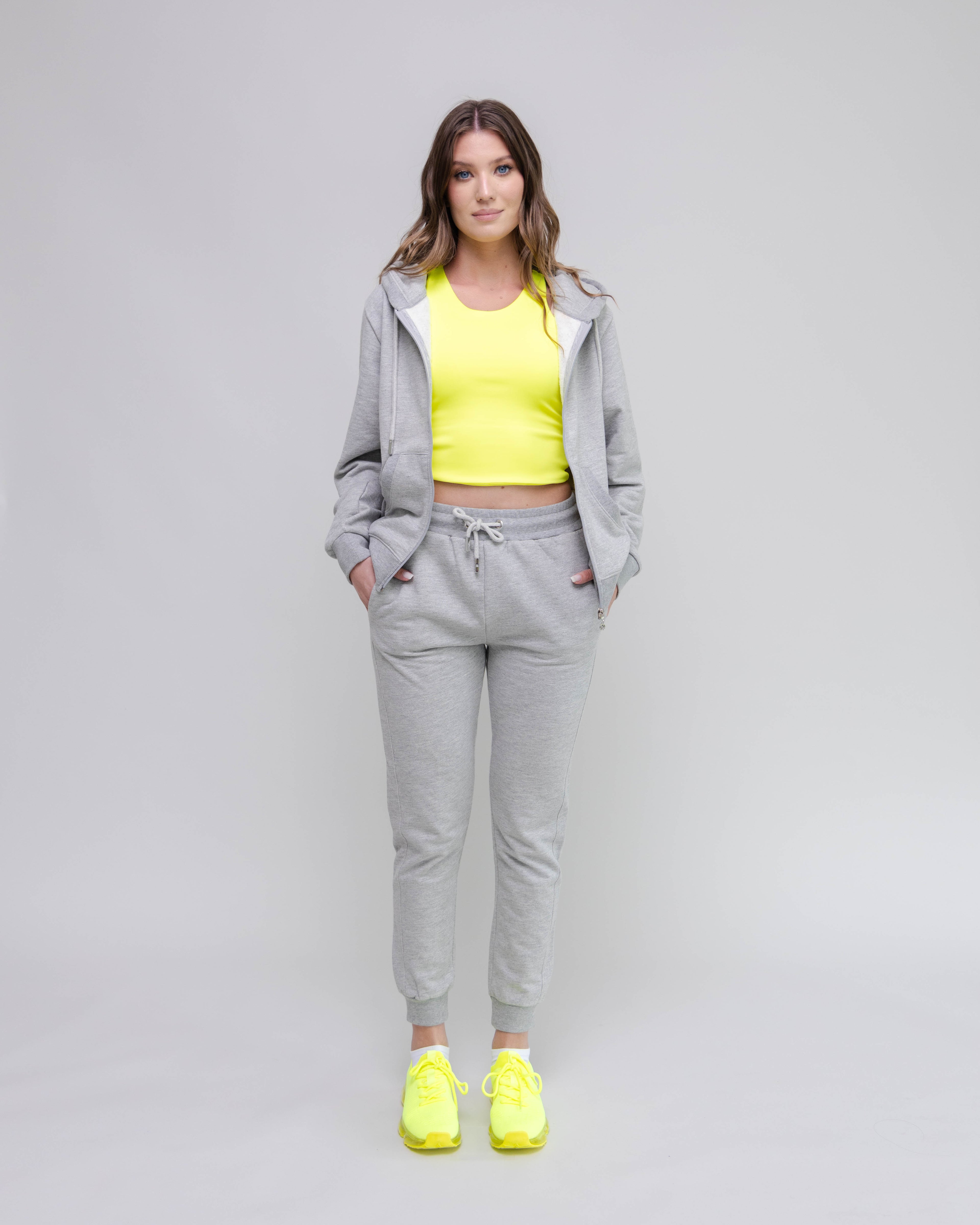 Woman wearing a gray tracksuit with a yellow top and shoes on a light gray background