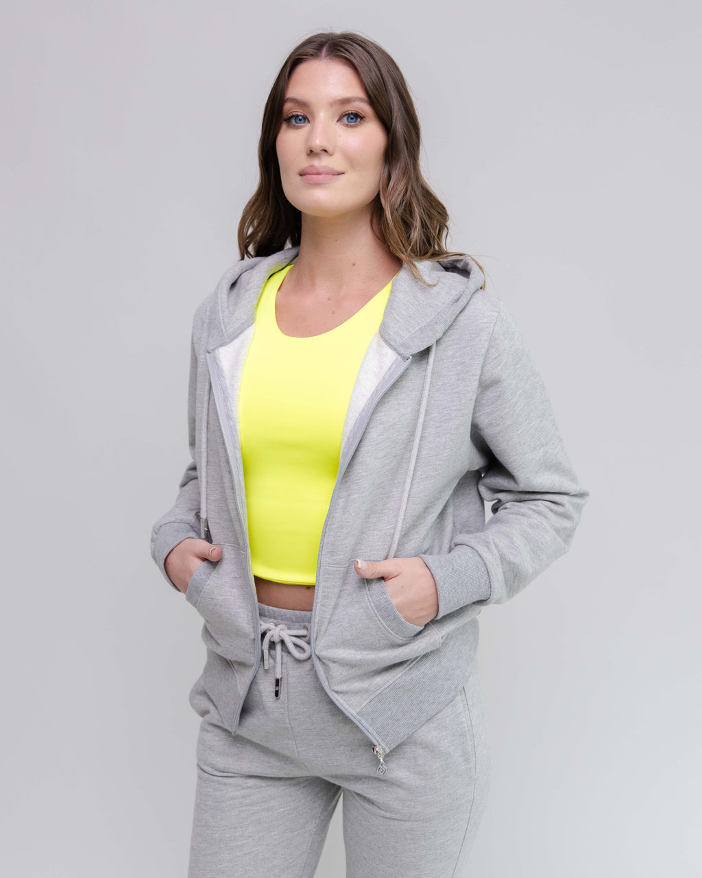 Woman wearing a gray tracksuit with a yellow top on a light gray background