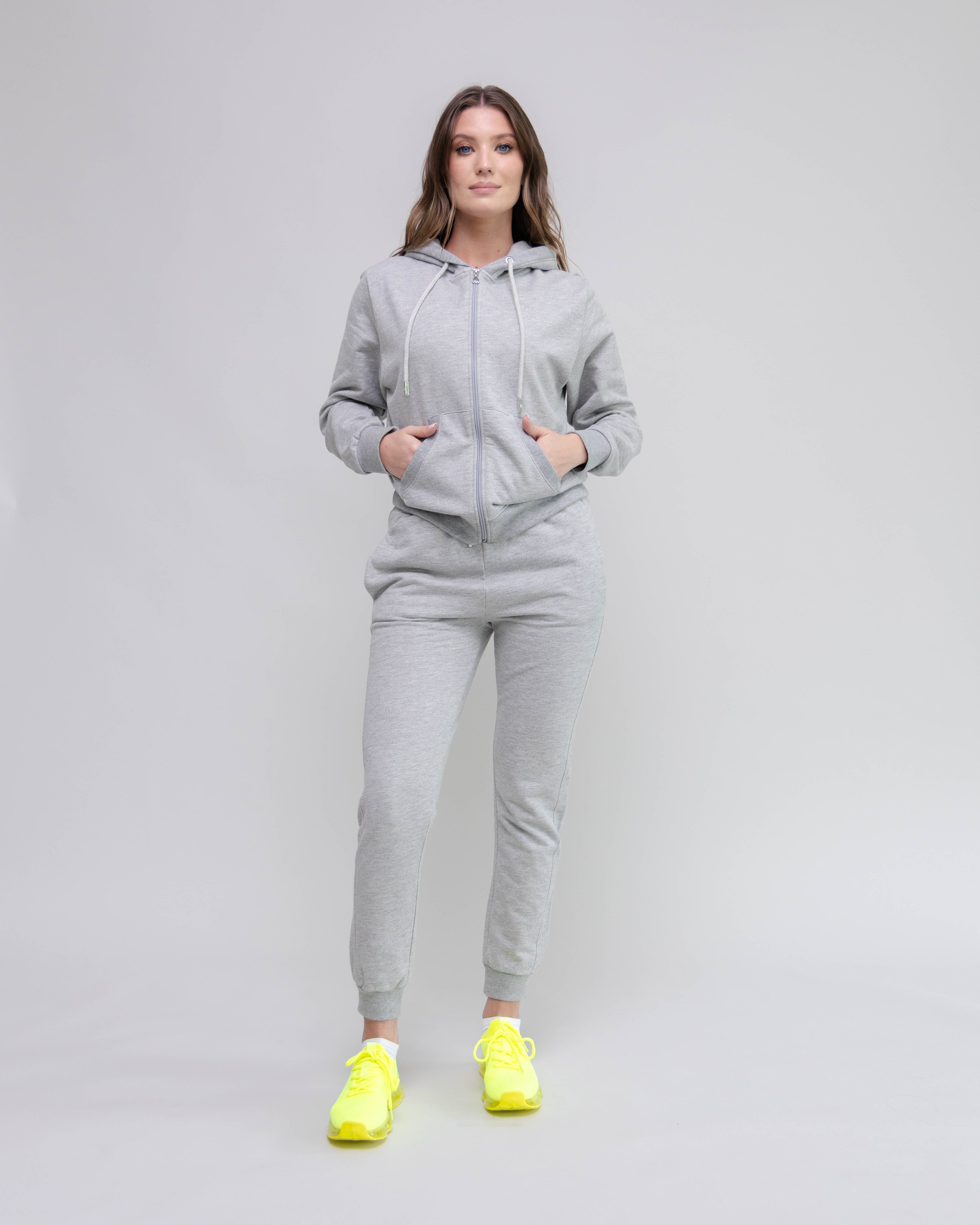 Woman wearing a gray tracksuit with yellow shoes on a plain background