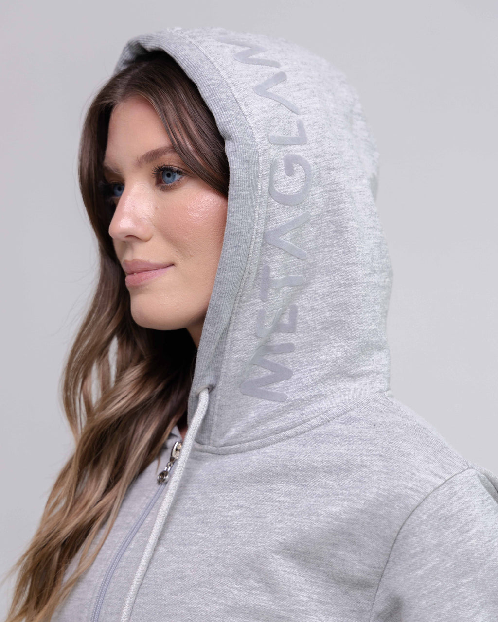 Woman wearing a gray hoodie with 'MENAG' branding on a light gray background