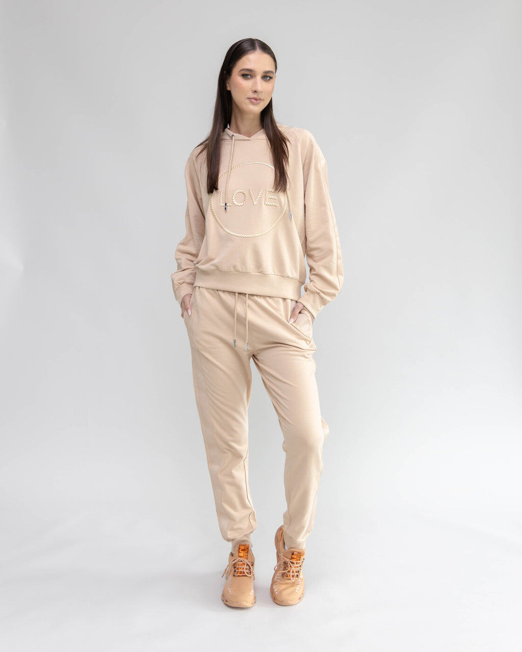 Woman wearing a beige tracksuit with 'LOVE' printed on the hoodie against a light gray background