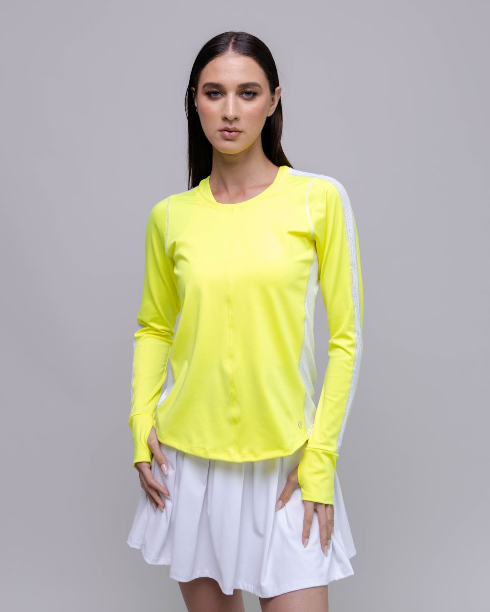 Woman wearing a bright yellow long-sleeve top and white skirt on a gray background