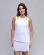 Woman wearing a white sleeveless top with yellow accents and a white skirt on a gray background