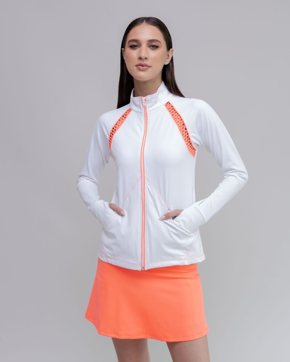 Woman wearing a white jacket with orange accents and an orange skirt on a gray background
