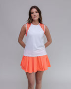 Woman wearing a white top with orange accents and an orange skirt on a gray background