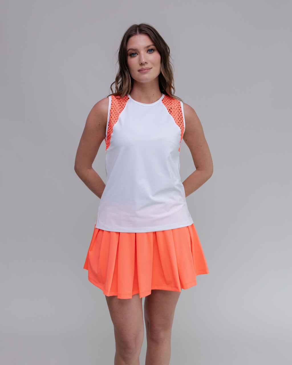 Woman wearing a white top with orange accents and an orange skirt on a gray background