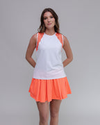 Woman wearing a white top with orange accents and an orange skirt on a gray background