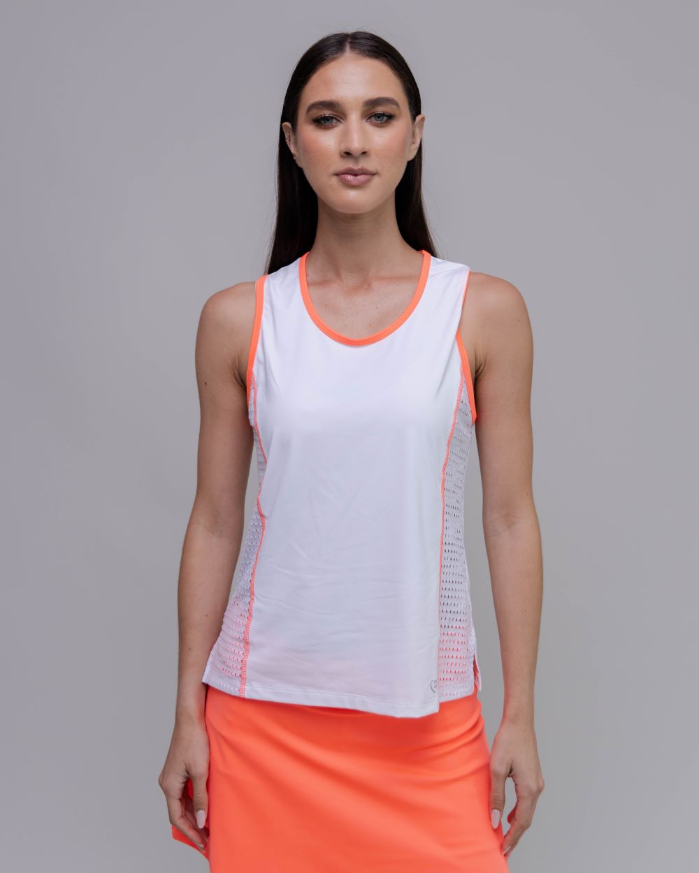 Woman wearing a white tank top with orange accents and an orange skirt on a gray background