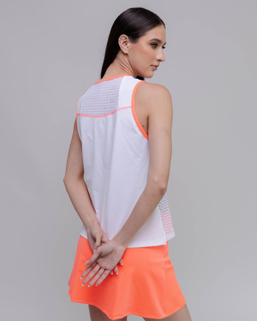 Woman wearing a white sleeveless top with pink accents and an orange skirt on a gray background