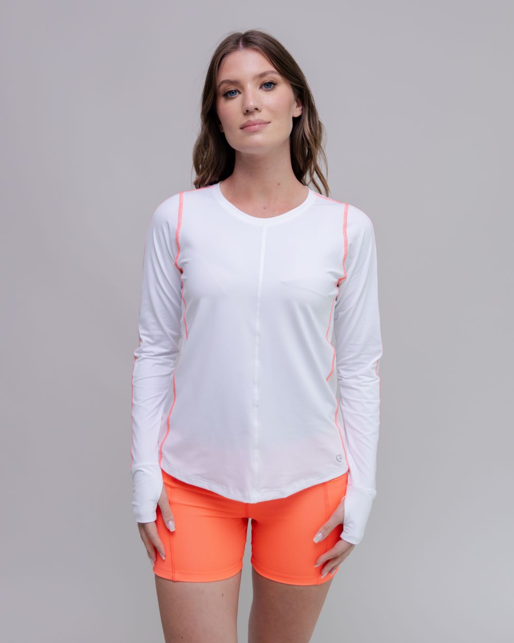 Woman wearing a white long-sleeve top and orange shorts on a gray background