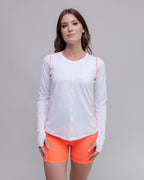 Woman wearing a white long-sleeve top and orange shorts on a gray background