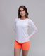 Woman wearing a white long-sleeve athletic top with pink accents and orange shorts on a gray background