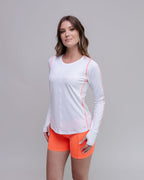 Woman wearing a white long-sleeve athletic top with orange accents and orange shorts on a gray background