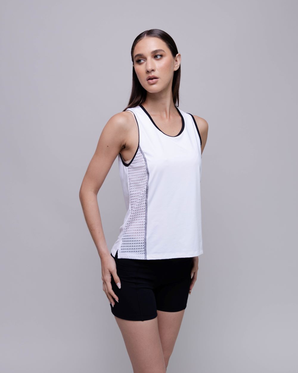 Woman wearing a white tank top with black accents and black shorts on a gray background