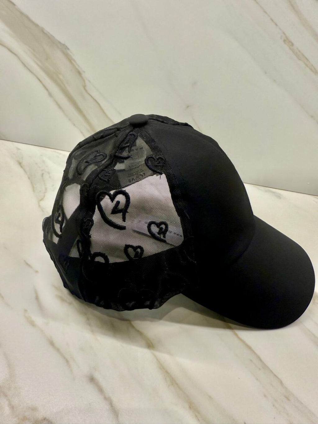 Black cap with heart patterns on a white marble surface