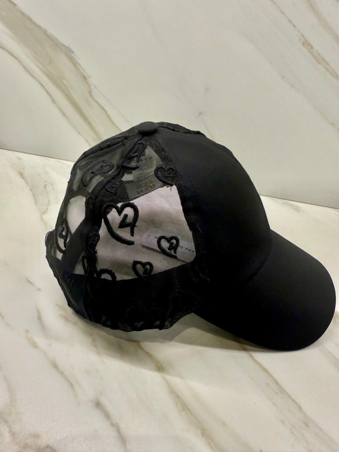 Black cap with heart patterns on a white marble surface